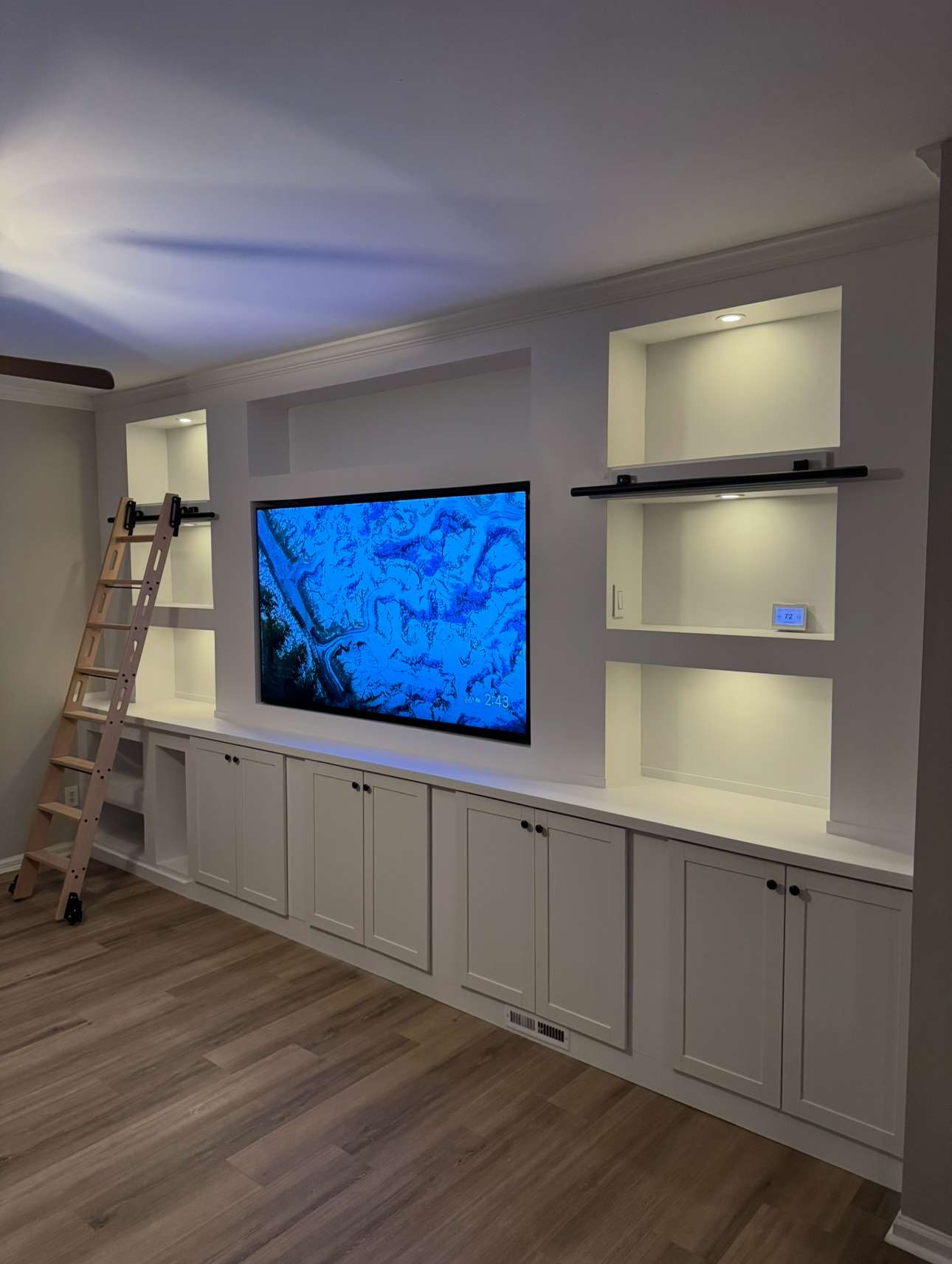 Floor-to-ceiling white built-in media wall with library ladder