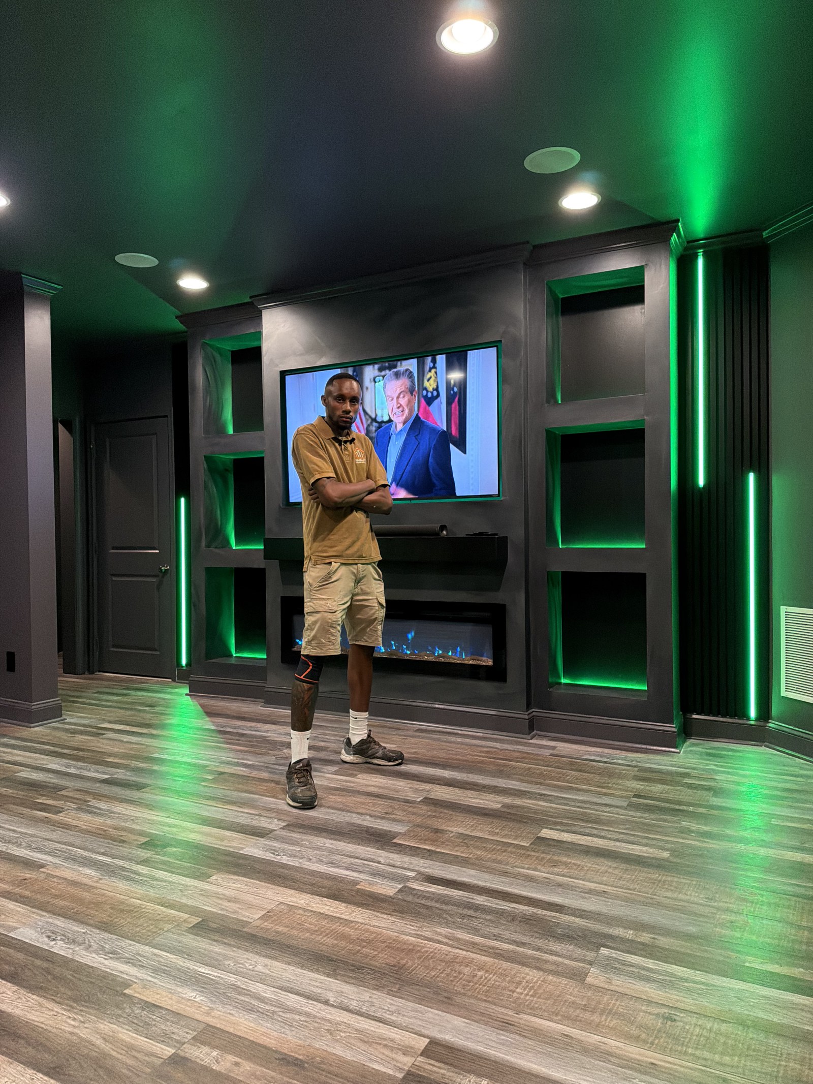 Jaquan Straughn — Founder, Quality Home Installs — standing beside a finished custom media wall